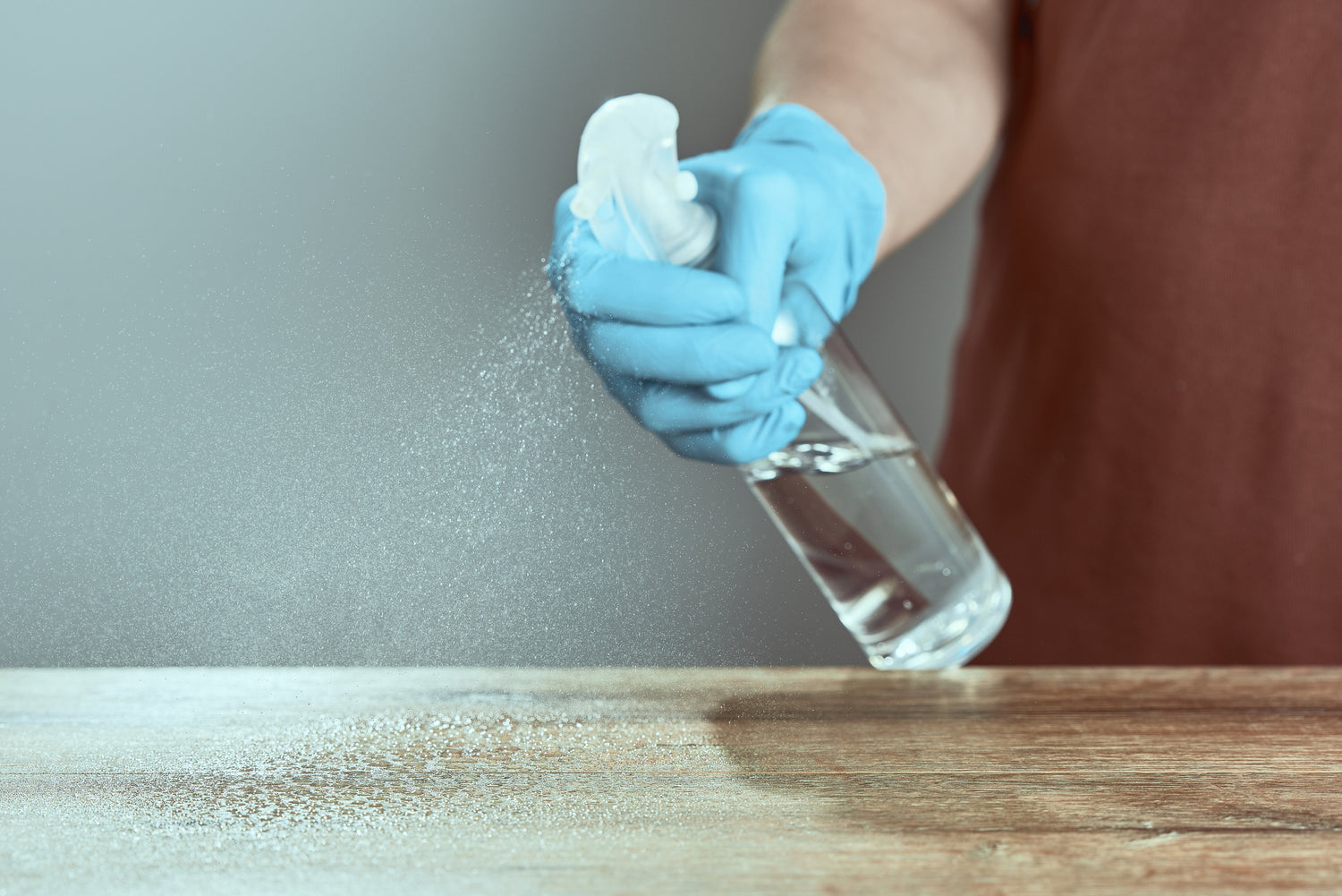 Person wearing blue gloves cleaning a wooden surface with a spray bottle containing Rely+On Virkon - effective against the widest known spectrum of pathogens